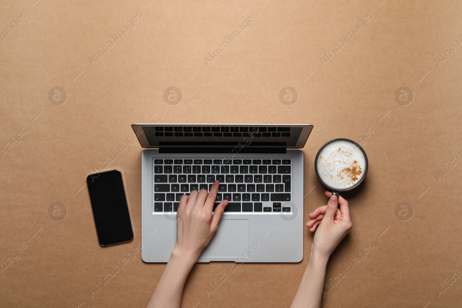Photo of Woman with cup of cappuccino using laptop at light brown table, top view. Space for text