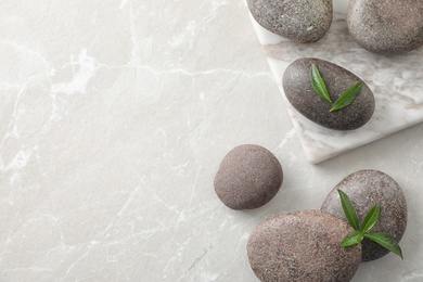 Flat lay composition with spa stones and green leaves on grey table, space for text