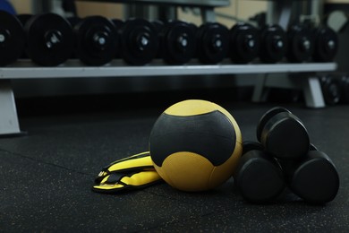 Photo of Yellow medicine ball, weighting agents and dumbbells on floor in gym, space for text