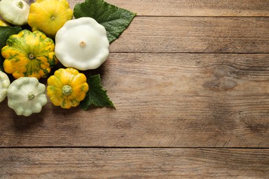 Fresh ripe pattypan squashes with leaves on wooden table, flat lay. Space for text