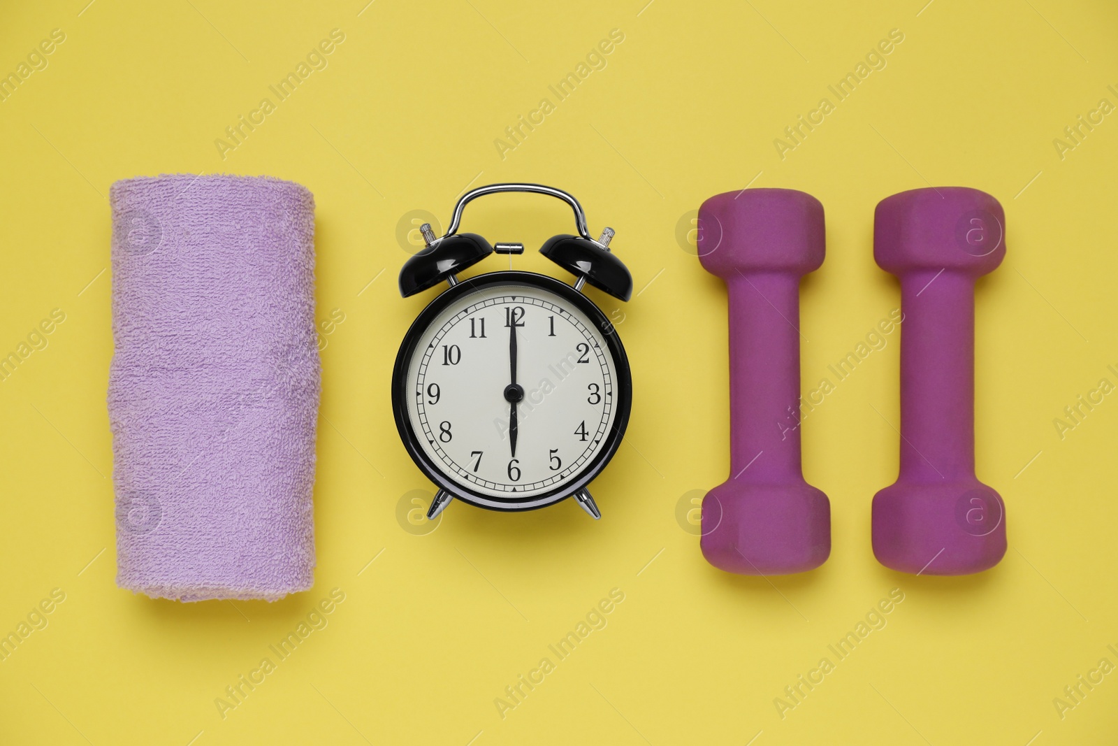 Photo of Alarm clock, towel and dumbbells on yellow background, flat lay. Morning exercise