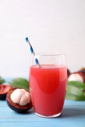 Photo of Delicious fresh mangosteen juice in glass on light blue wooden table