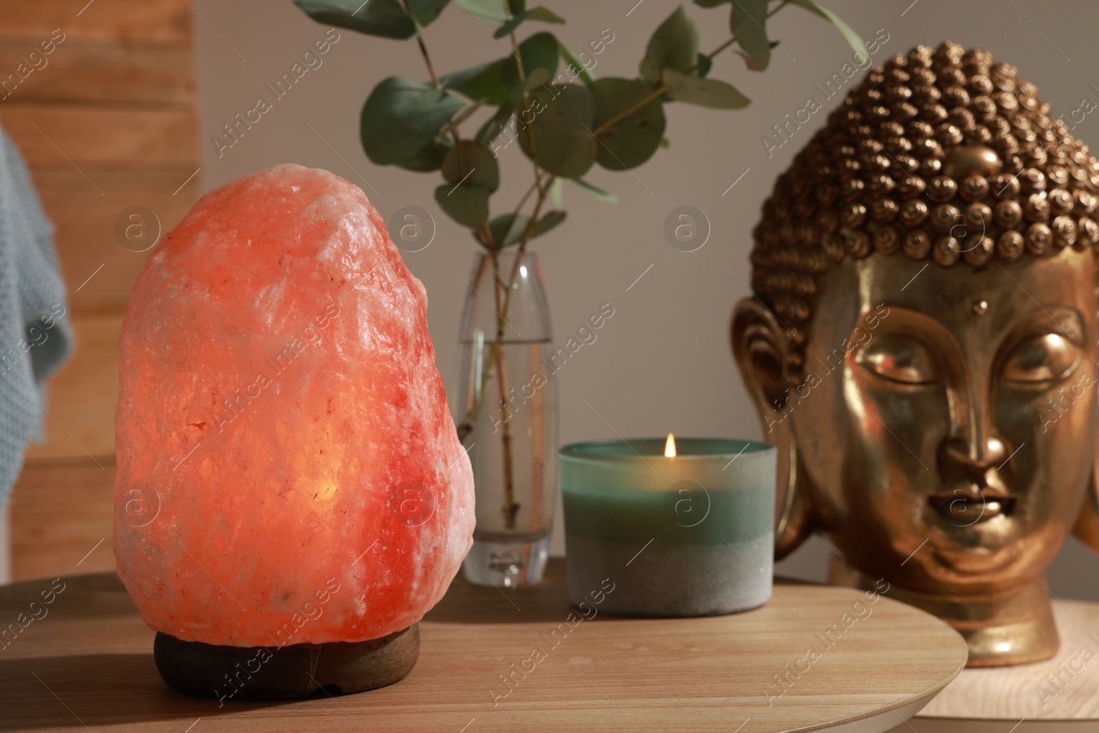 Photo of Beautiful Himalayan salt lamp, golden Buddha sculpture and decor on wooden tables indoors