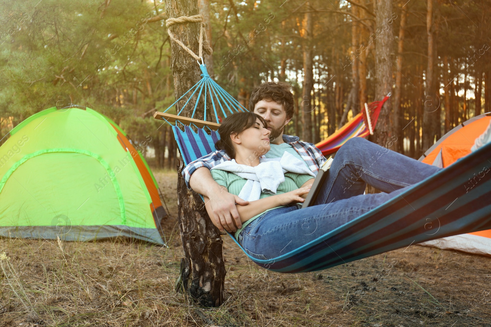 Photo of Lovely couple with book resting in comfortable hammock outdoors