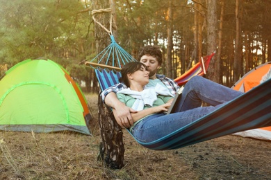 Lovely couple with book resting in comfortable hammock outdoors