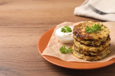 Photo of Delicious zucchini pancakes and bowl with sour cream on wooden table. Space for text