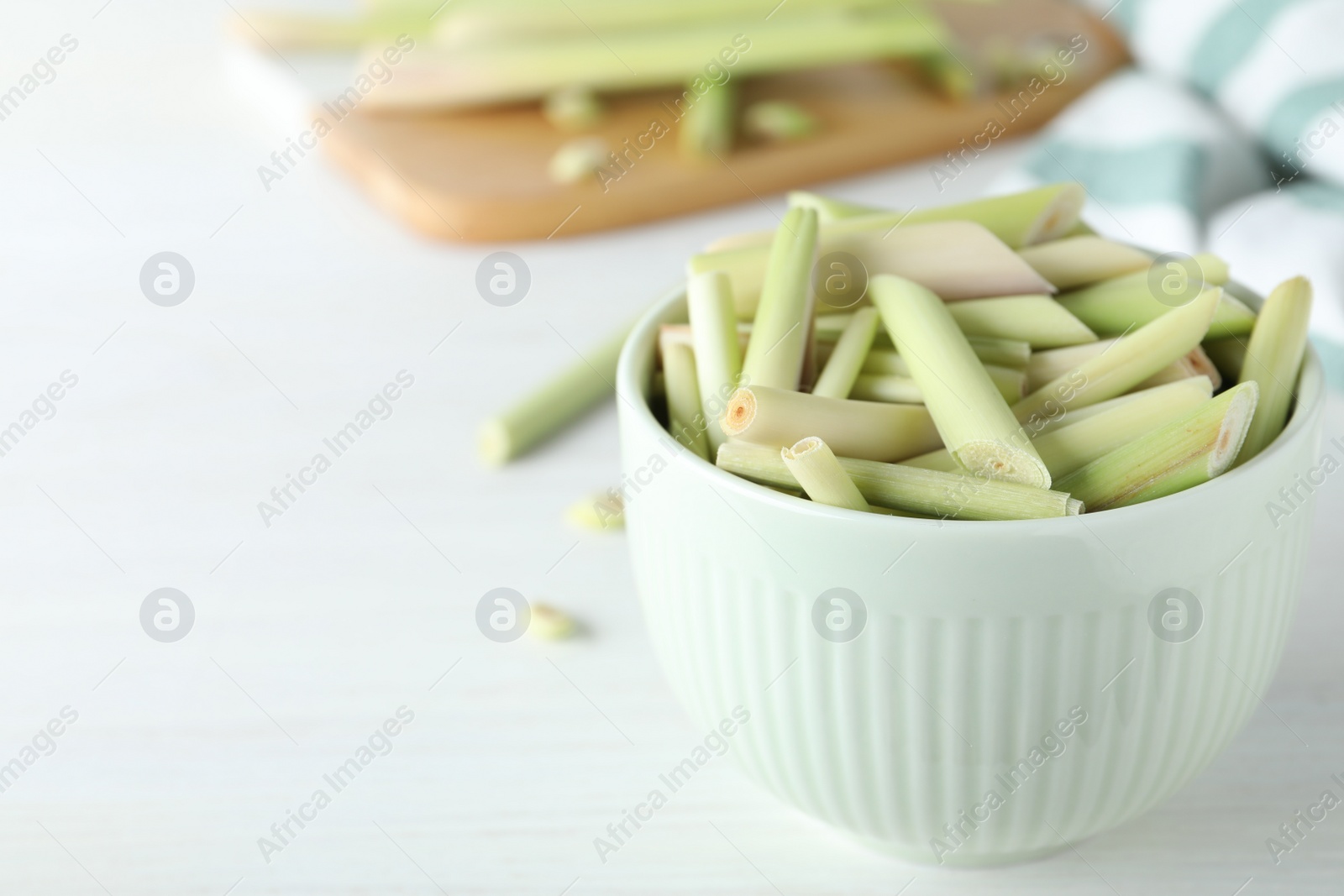 Photo of Bowl with fresh lemongrass stalks on white table, closeup. Space for text