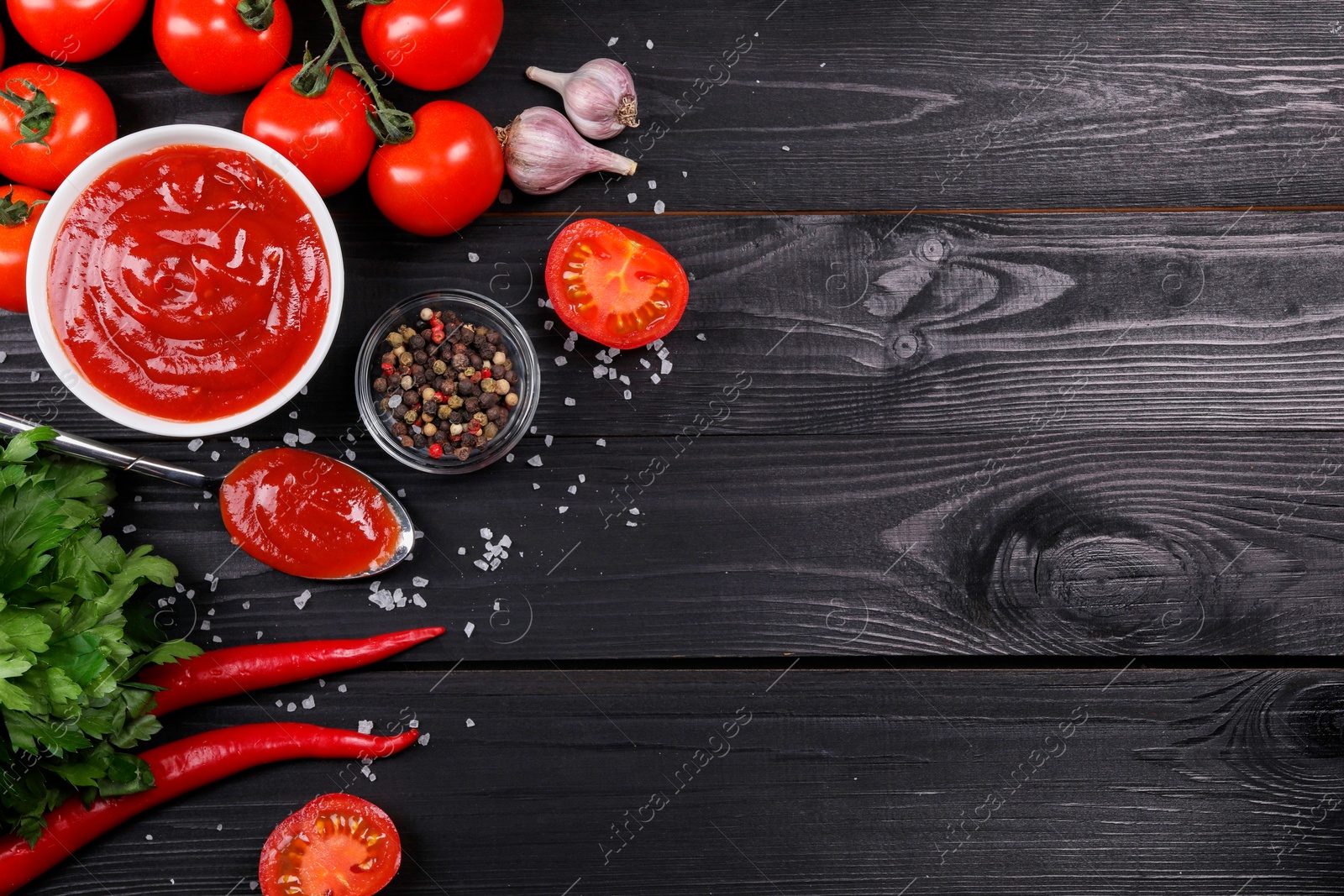 Photo of Flat lay composition with delicious ketchup, spices and products on black wooden table, space for text. Tomato sauce