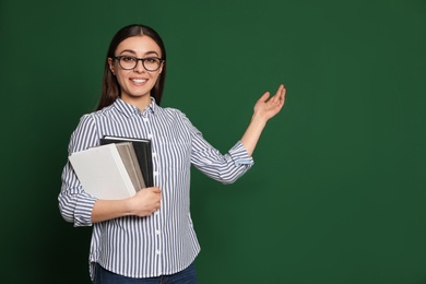 Portrait of young teacher with notebooks on green background. Space for text