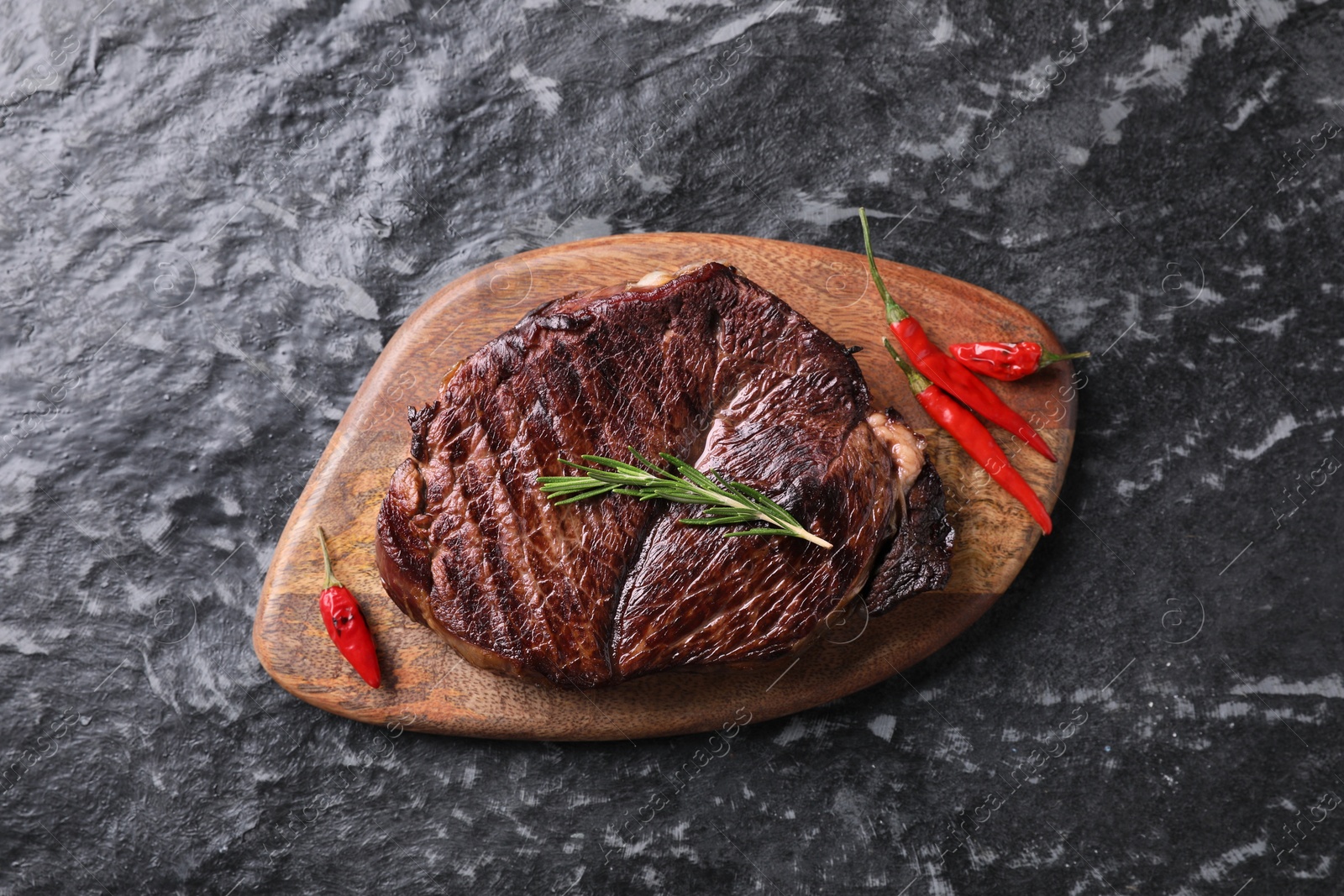 Photo of Delicious fried beef meat with pepper and rosemary on grey textured table, top view