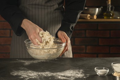 Photo of Making bread. Woman preparing dough in bowl at grey textured table in kitchen, closeup