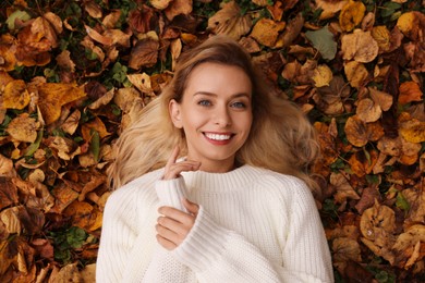 Smiling woman lying among autumn leaves outdoors, top view