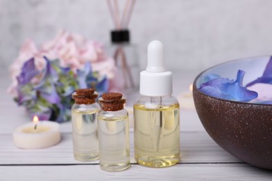 Photo of Spa composition. Bottles of essential oil and aromatic water with flowers in bowl on white wooden table, closeup