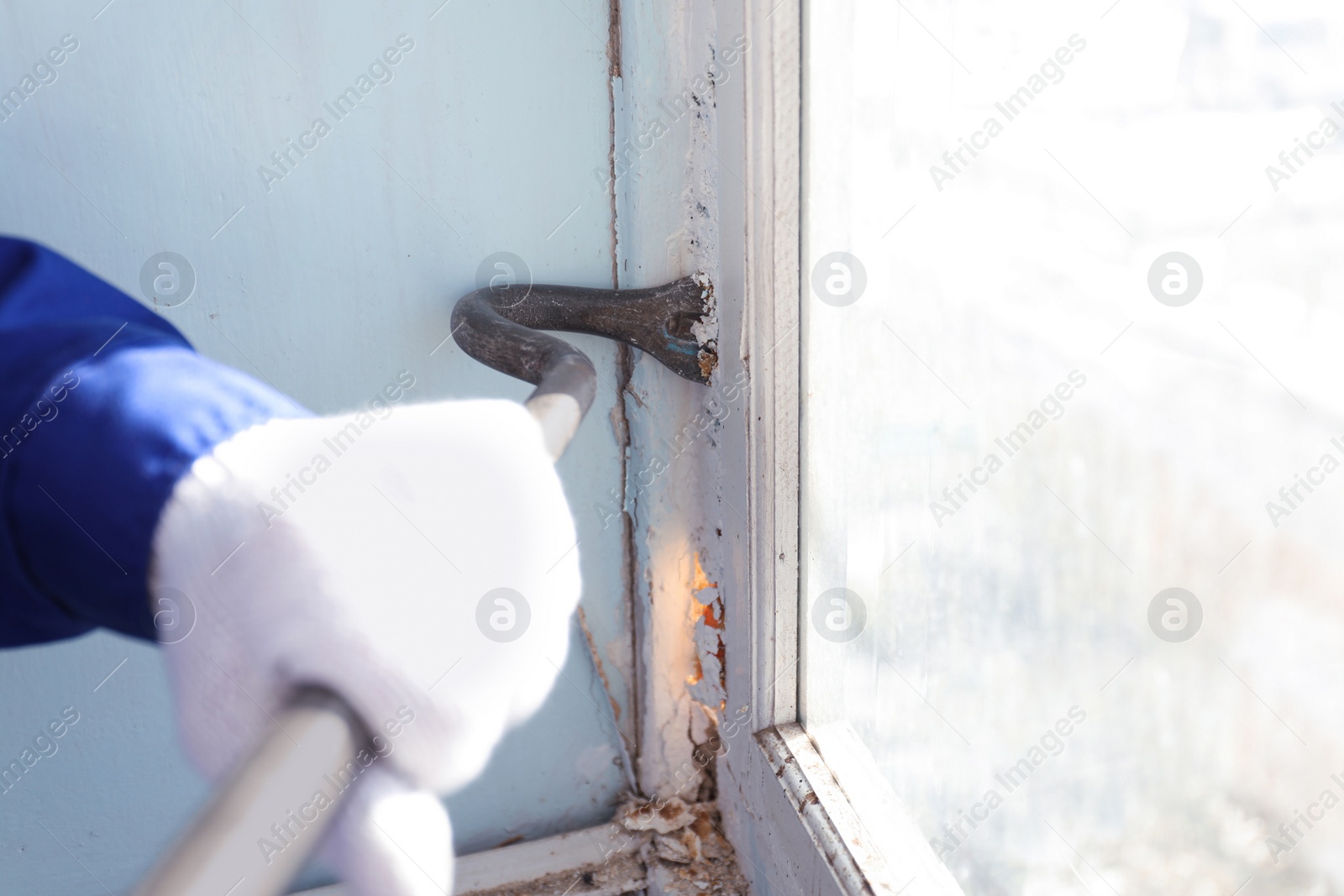 Photo of Worker dismantling old window with crowbar indoors, closeup