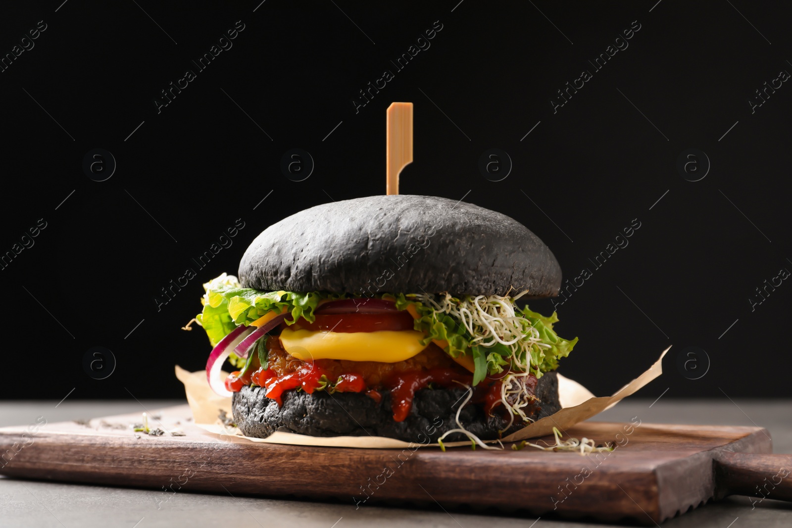 Photo of Board with tasty black vegetarian burger on table against dark background