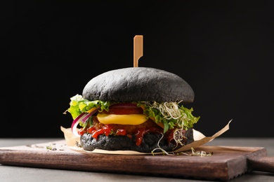 Photo of Board with tasty black vegetarian burger on table against dark background