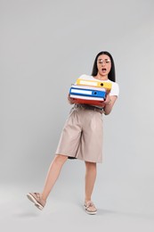 Stressful woman with folders walking on light gray background