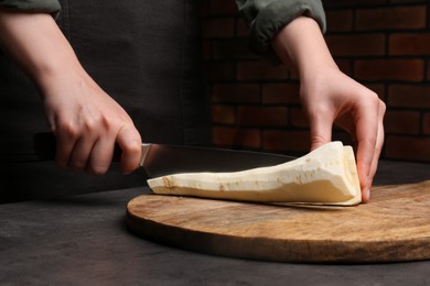 Photo of Woman cutting delicious fresh ripe parsnip at black table, closeup