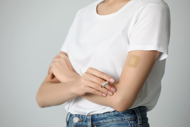 Photo of Young woman with nicotine patch and cigarette on light grey background, closeup