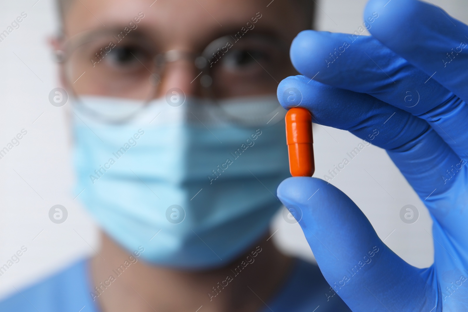 Photo of Doctor holding pill on light background, selective focus. Space for text