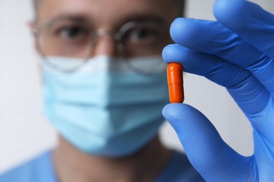 Doctor holding pill on light background, selective focus. Space for text