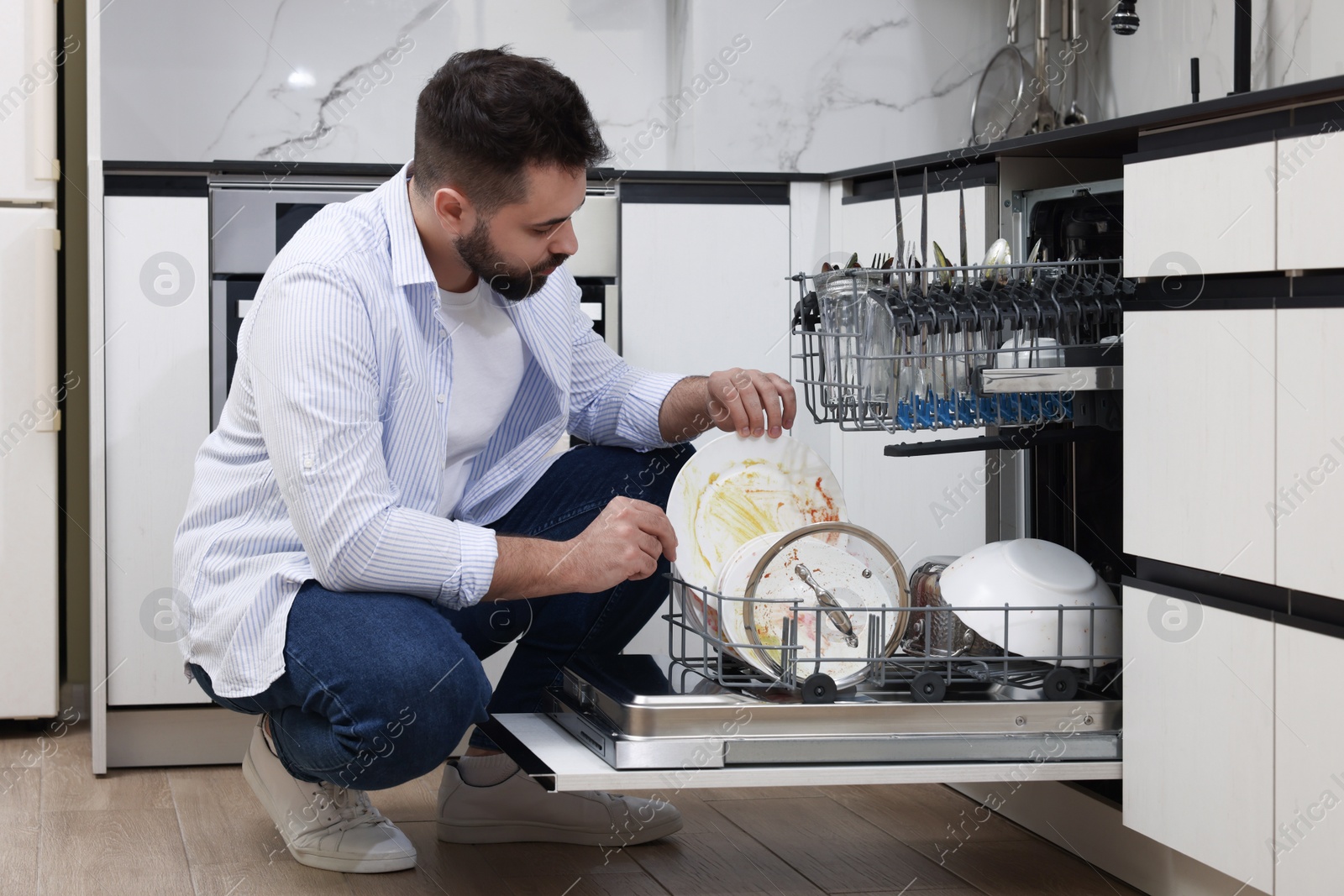 Photo of Man loading dishwasher with dirty plates indoors