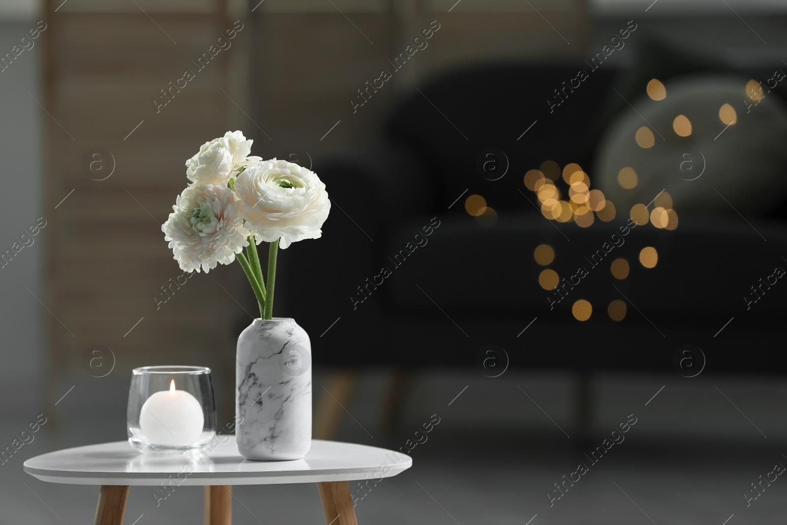 Photo of Vase with beautiful white flowers and burning candle on table in room, bokeh effect. Stylish interior design