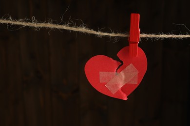 Photo of Broken heart. Torn red paper heart with medical adhesive bandages on dark background, space for text