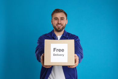Photo of Male courier holding parcel with sticker Free Delivery on light blue background