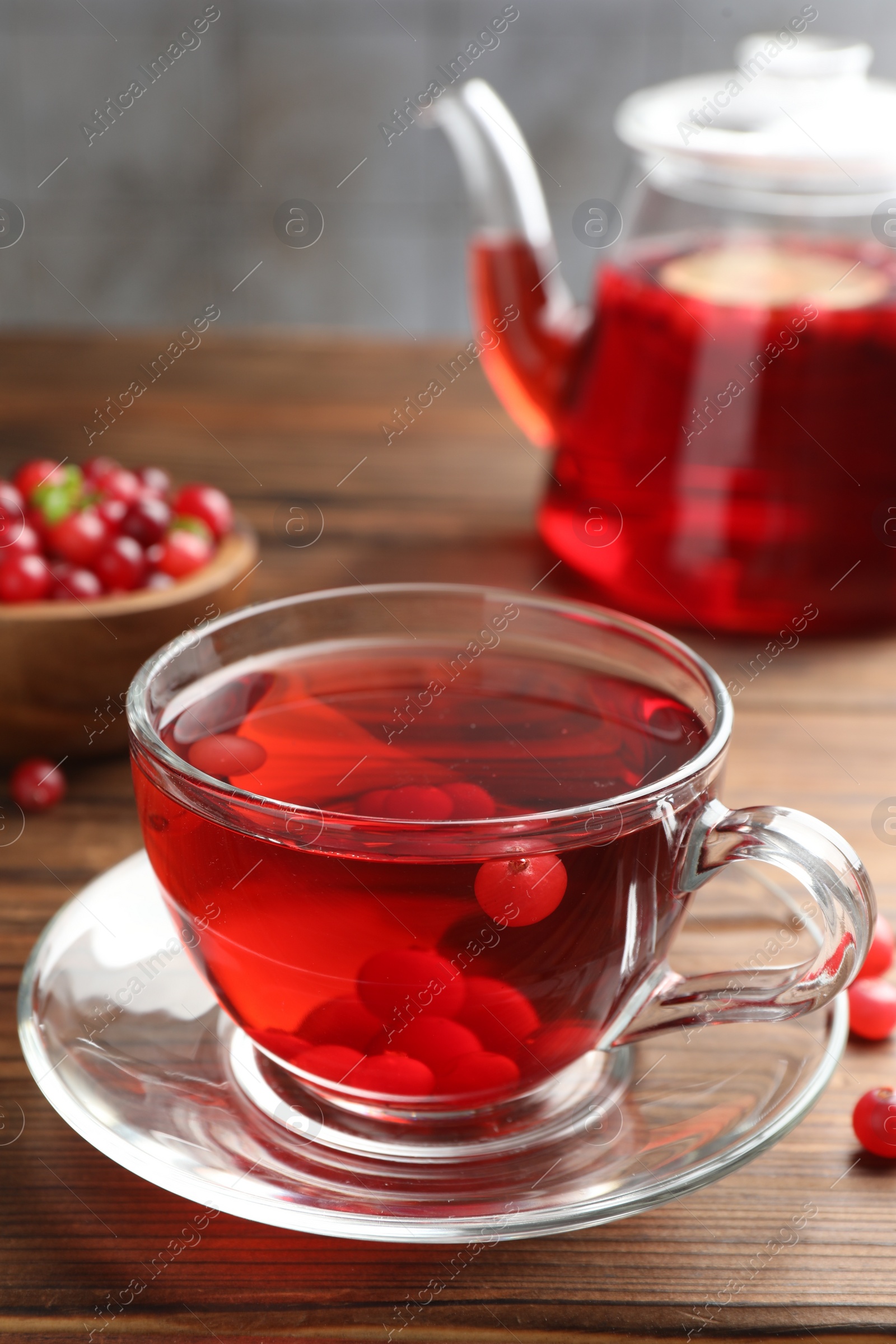 Photo of Tasty hot cranberry tea in glass cup and fresh berries on wooden table