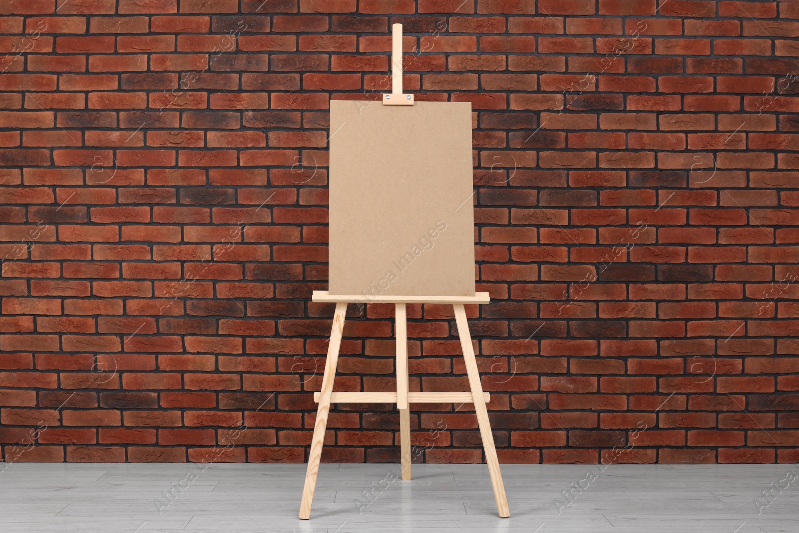 Photo of Wooden easel with blank board near brick wall indoors