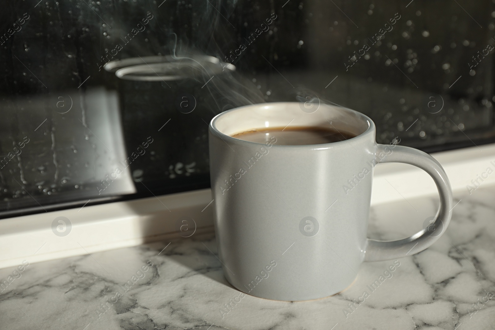 Photo of Cup of hot drink on window sill against glass with rain drops, space for text