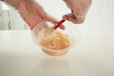 Photo of Woman preparing hair dye in bowl at white table, closeup