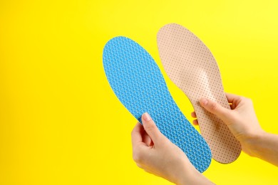 Photo of Woman holding insoles on yellow background, closeup. Space for text