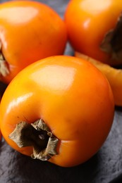 Photo of Delicious ripe persimmons on dark textured table, closeup