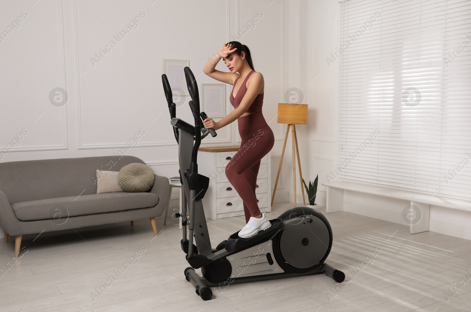 Photo of Young woman feeling tired of training on 	
elliptical machine at home