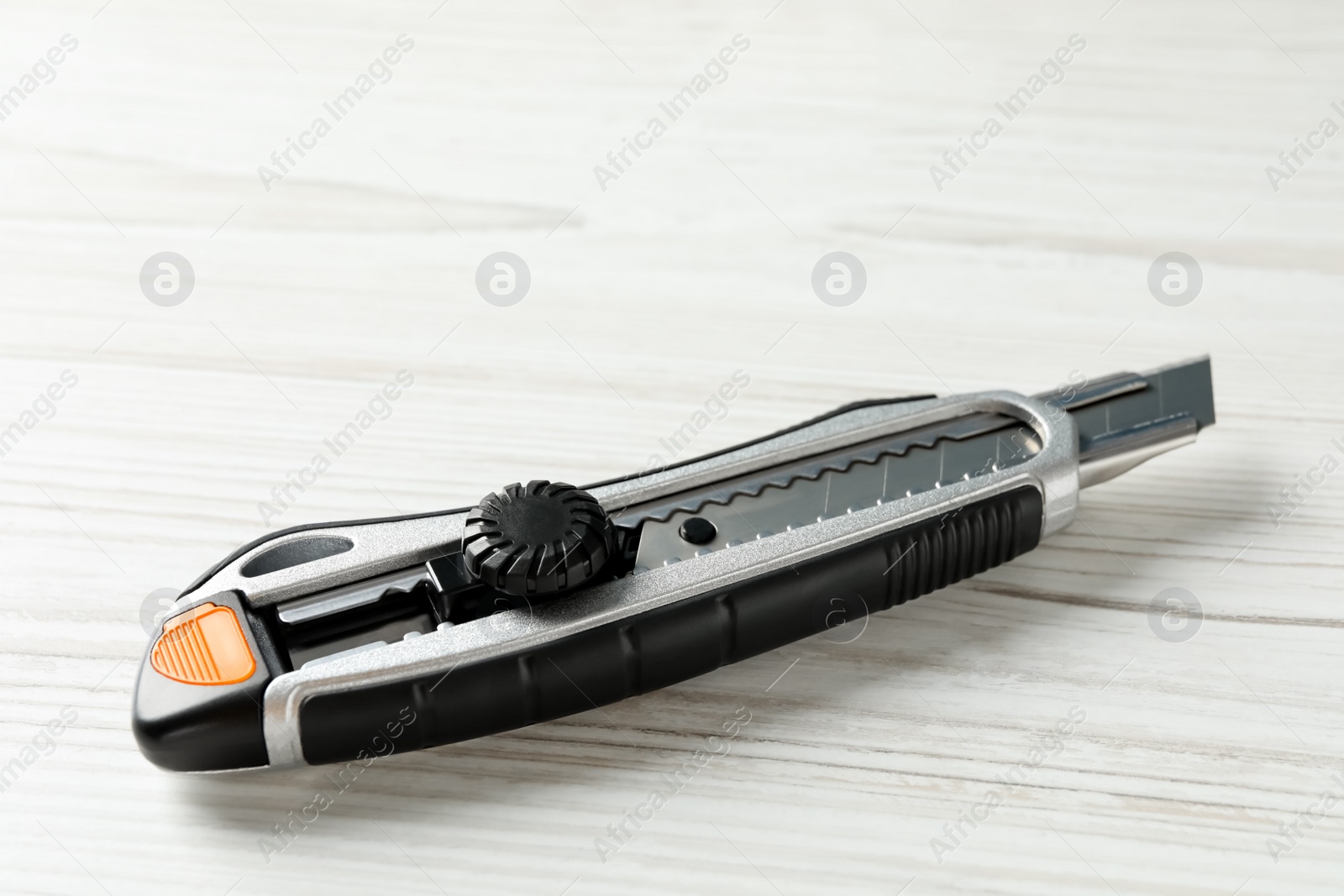 Photo of Utility knife on white wooden table. Construction tool