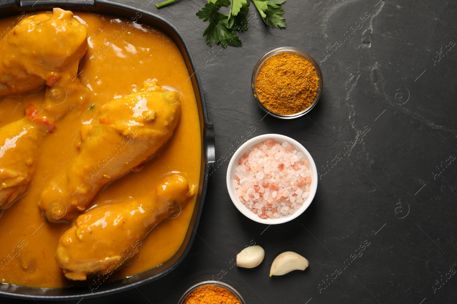 Photo of Tasty chicken curry and ingredients on black textured table, flat lay. Space for text