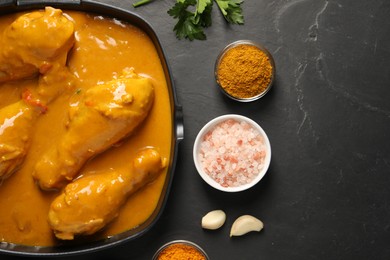 Tasty chicken curry and ingredients on black textured table, flat lay. Space for text