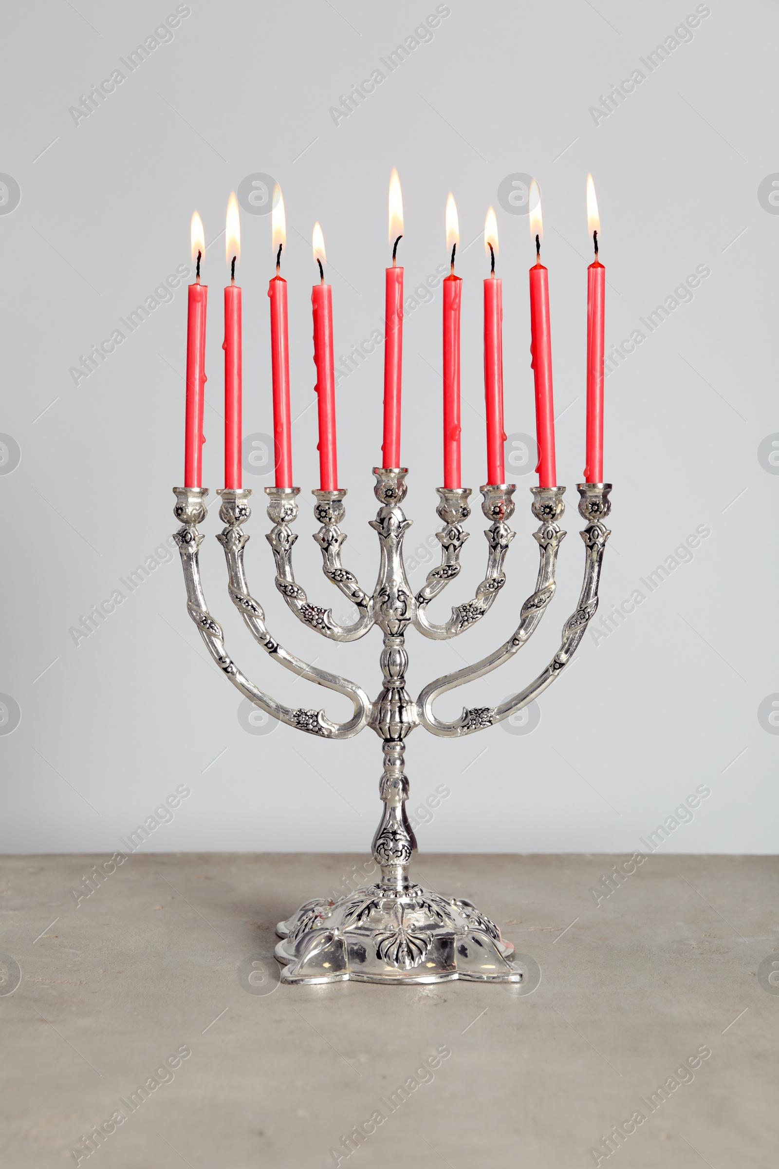 Photo of Silver menorah with burning candles on table against light grey background. Hanukkah celebration