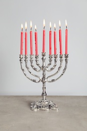 Silver menorah with burning candles on table against light grey background. Hanukkah celebration