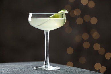 Glass of tasty cucumber martini on grey table against blurred lights, space for text