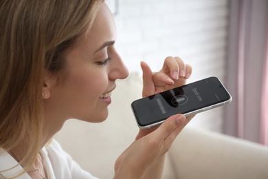 Photo of Young woman using voice search on smartphone indoors, closeup