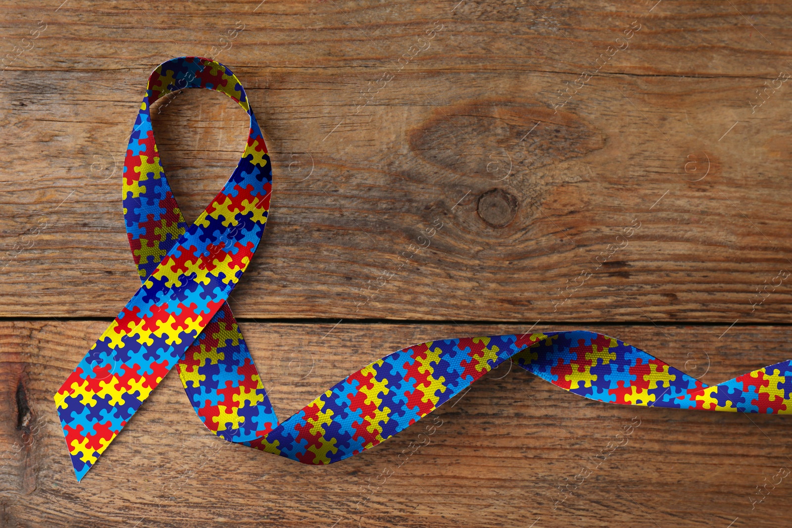 Image of World Autism Awareness Day. Colorful puzzle ribbon on wooden background, top view