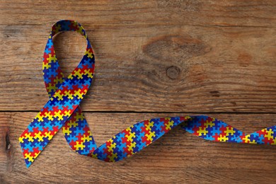 Image of World Autism Awareness Day. Colorful puzzle ribbon on wooden background, top view