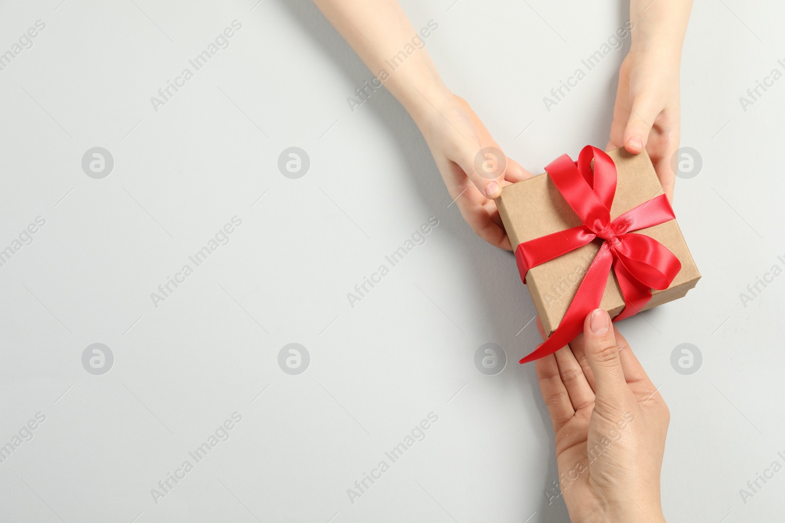Photo of Mother giving gift box to her child on white background, top view. Space for text
