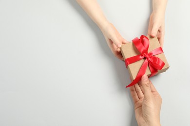 Mother giving gift box to her child on white background, top view. Space for text