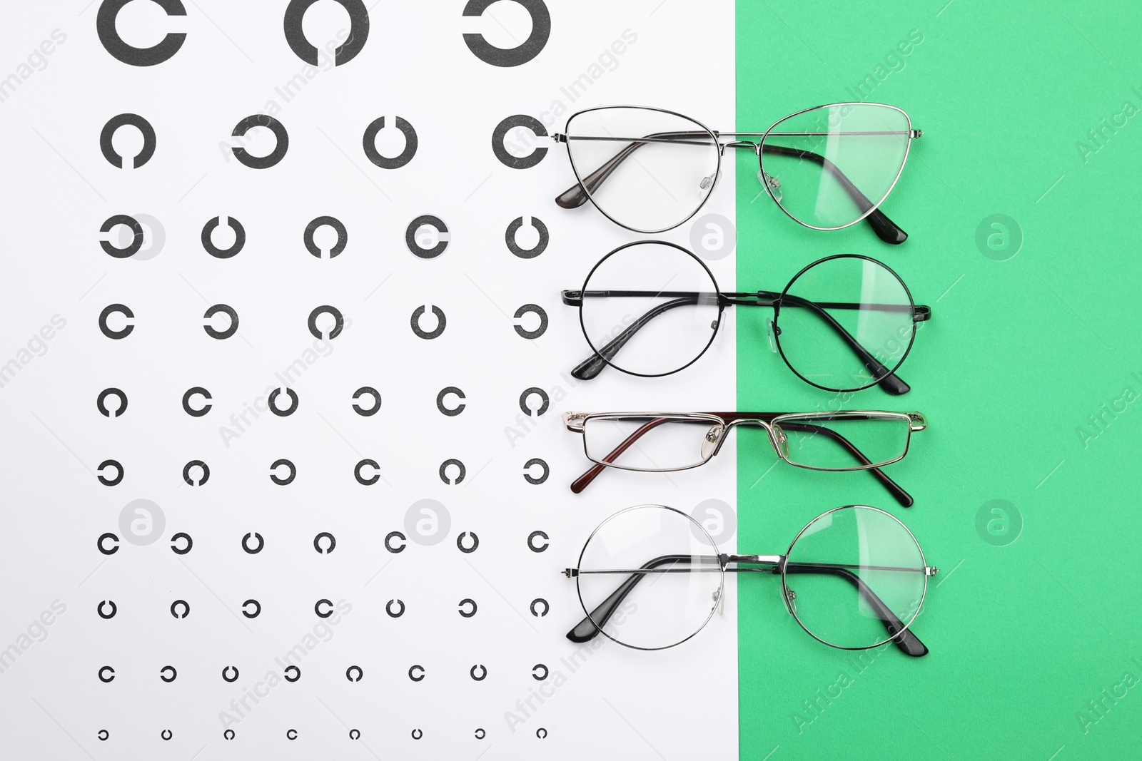 Photo of Vision test chart and glasses on green background, flat lay