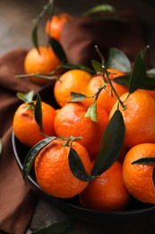 Photo of Fresh ripe tangerines with green leaves in bowl on table, closeup