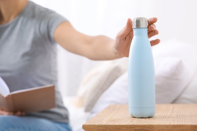 Photo of Woman with book taking thermo bottle in bedroom, closeup